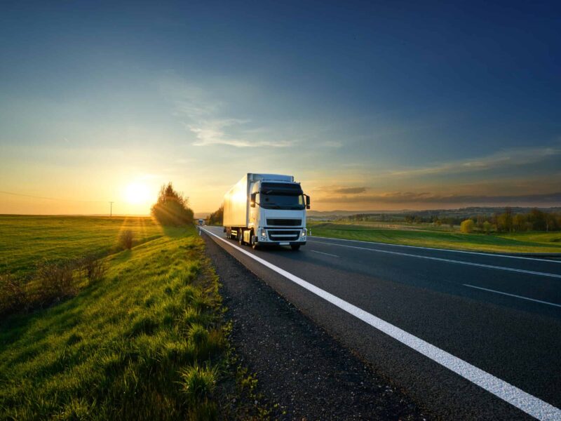 White truck driving on the road in landscape at sunset